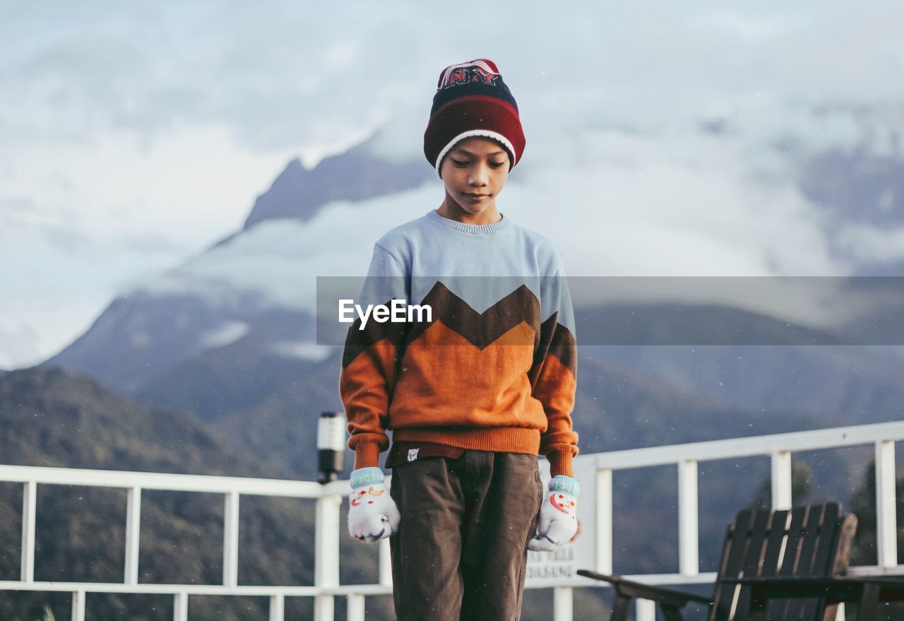 PORTRAIT OF MAN STANDING ON RAILING AGAINST MOUNTAIN