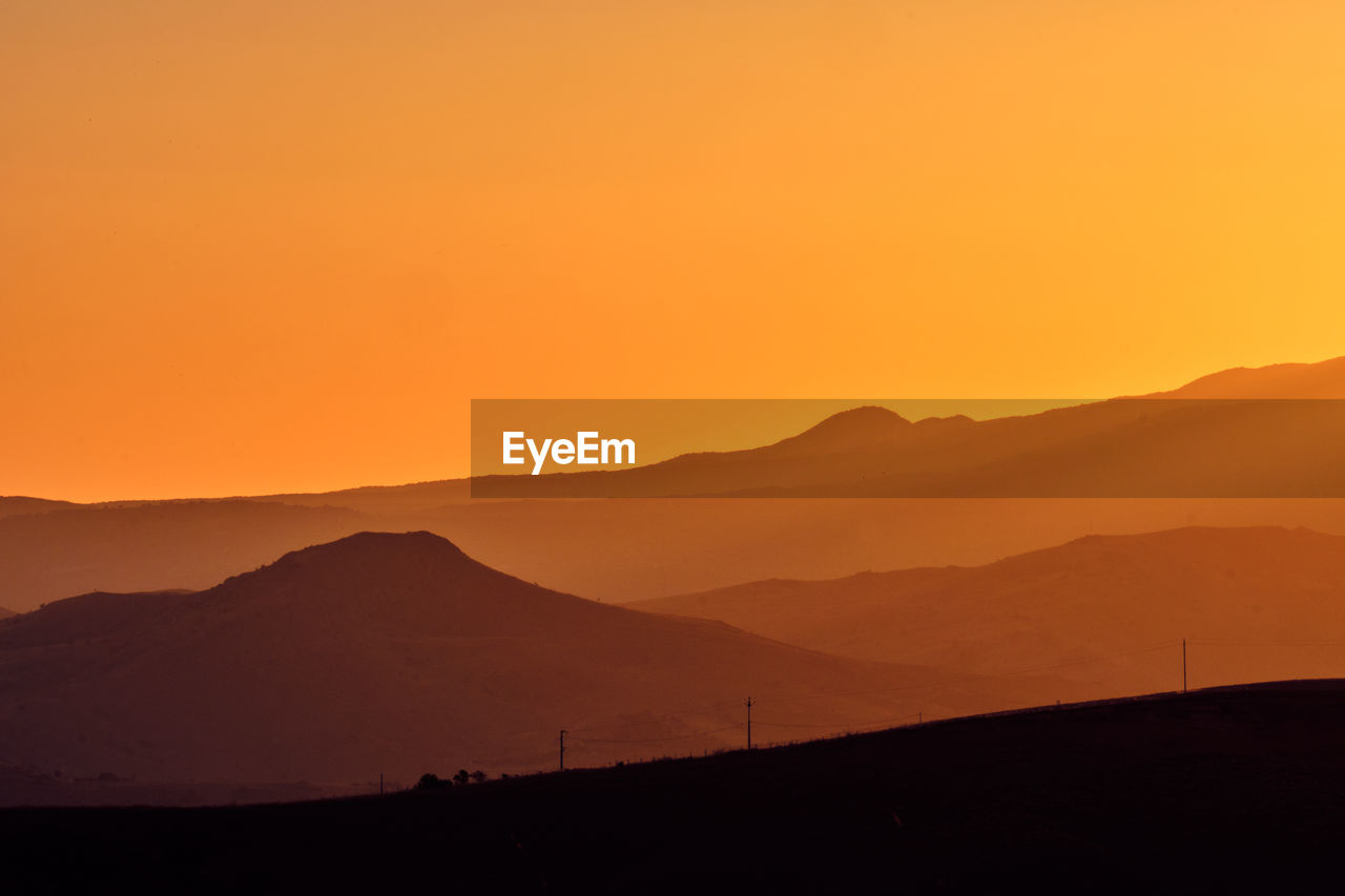 Scenic view of silhouette mountains against orange sky