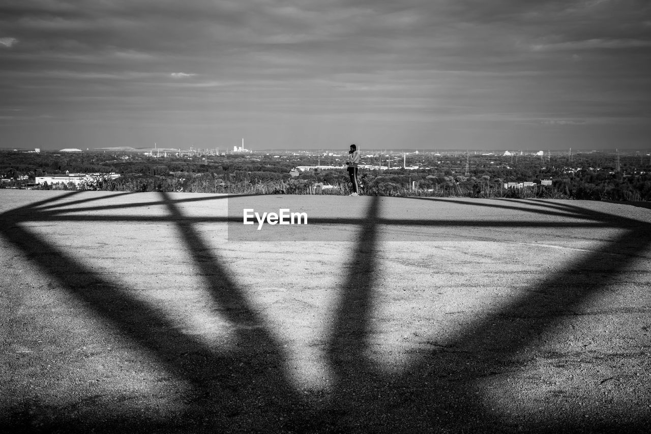 SHADOW OF MAN AND CITYSCAPE ON WALL AGAINST SKY