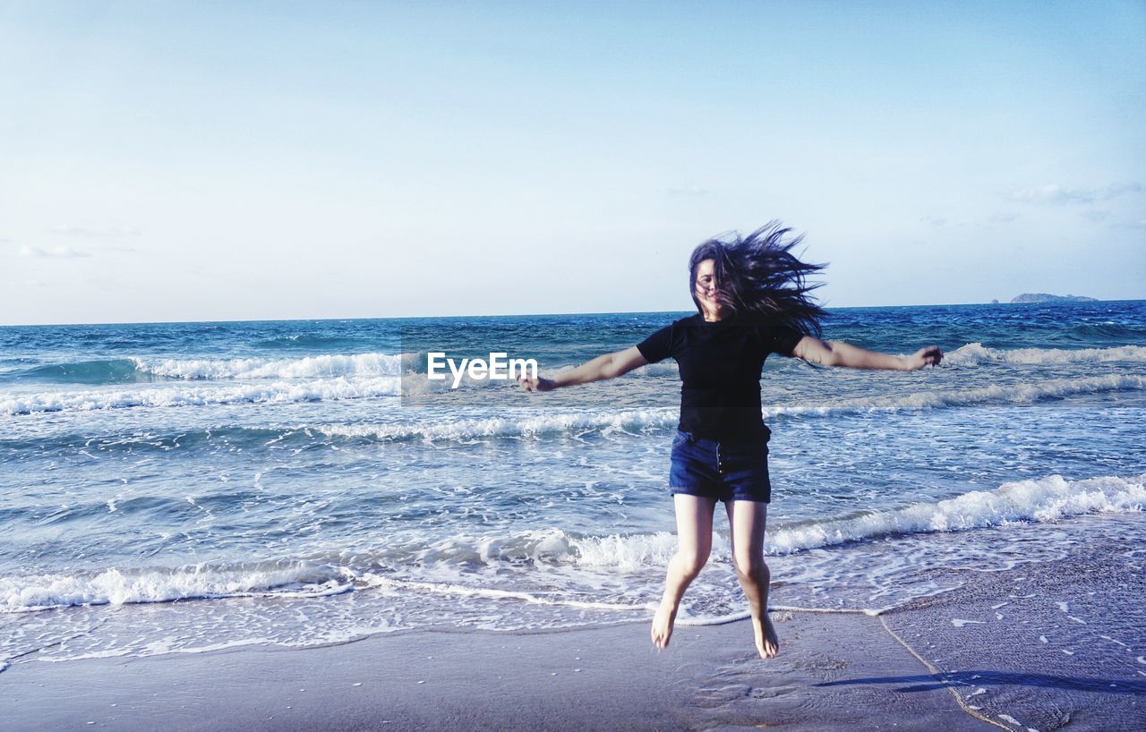 FULL LENGTH OF WOMAN WALKING ON BEACH AGAINST SEA