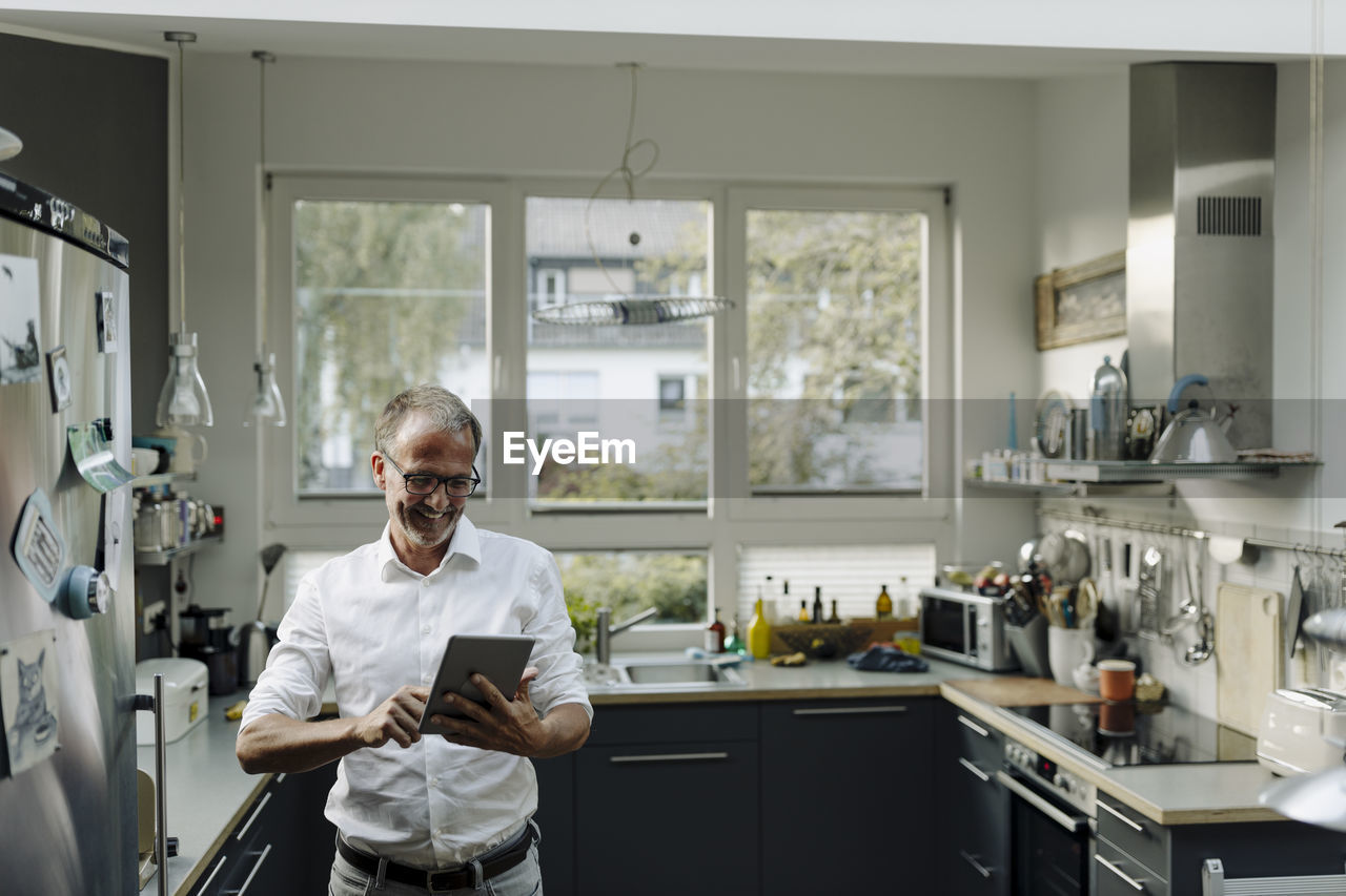 Mature man using digital tablet while standing in kitchen at home