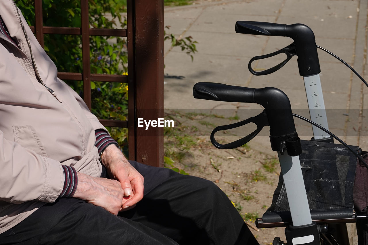 Midsection of man with mobility walker sitting outdoors