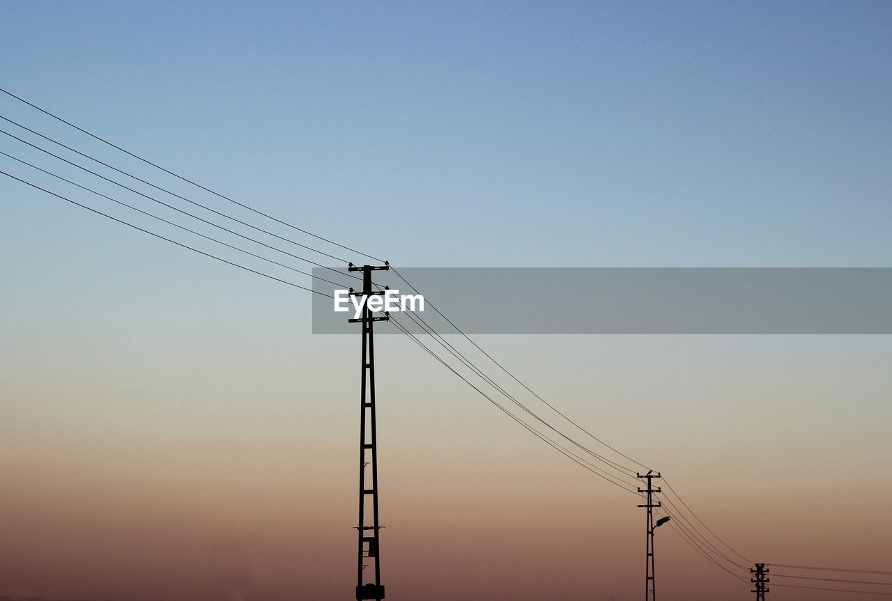Low angle view of silhouette electricity pylon against gradient sky