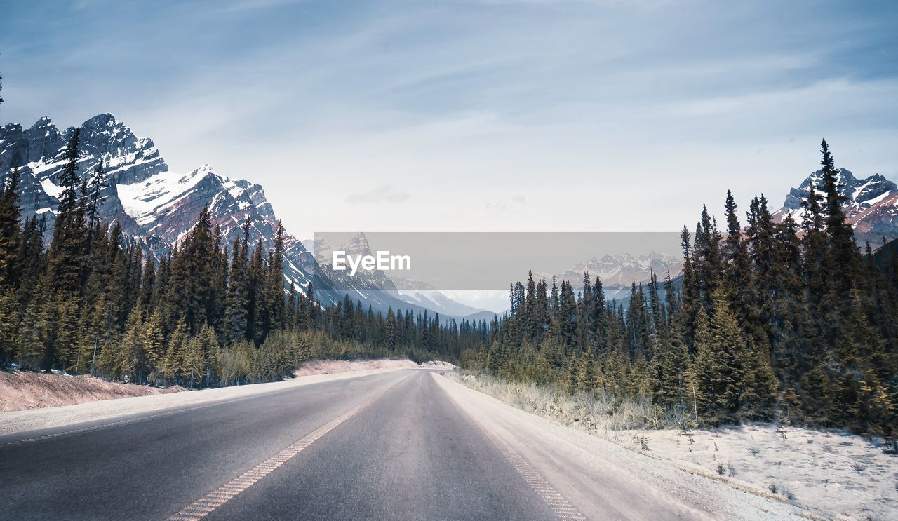 Road amidst trees and snowcapped mountains against sky