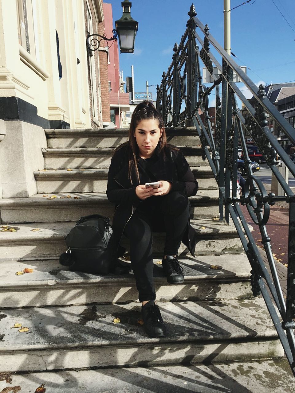 Portrait of young woman using mobile phone while sitting on steps in city