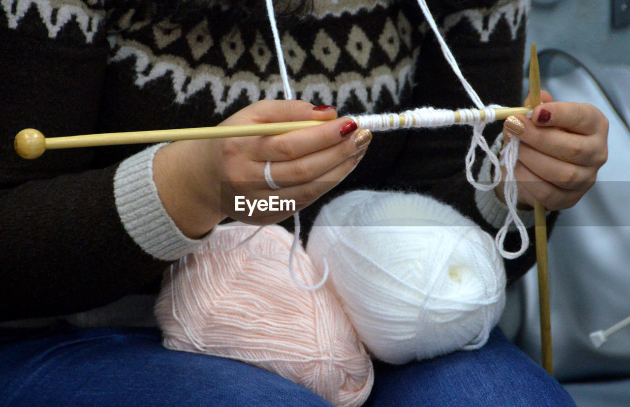 Midsection of woman knitting wool at home