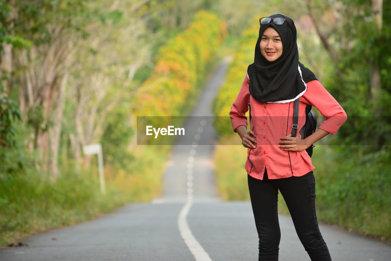 Portrait of young woman with hands on hip standing on road