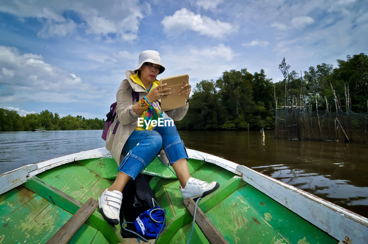 Full length of woman using mobile phone while sitting on rowboat