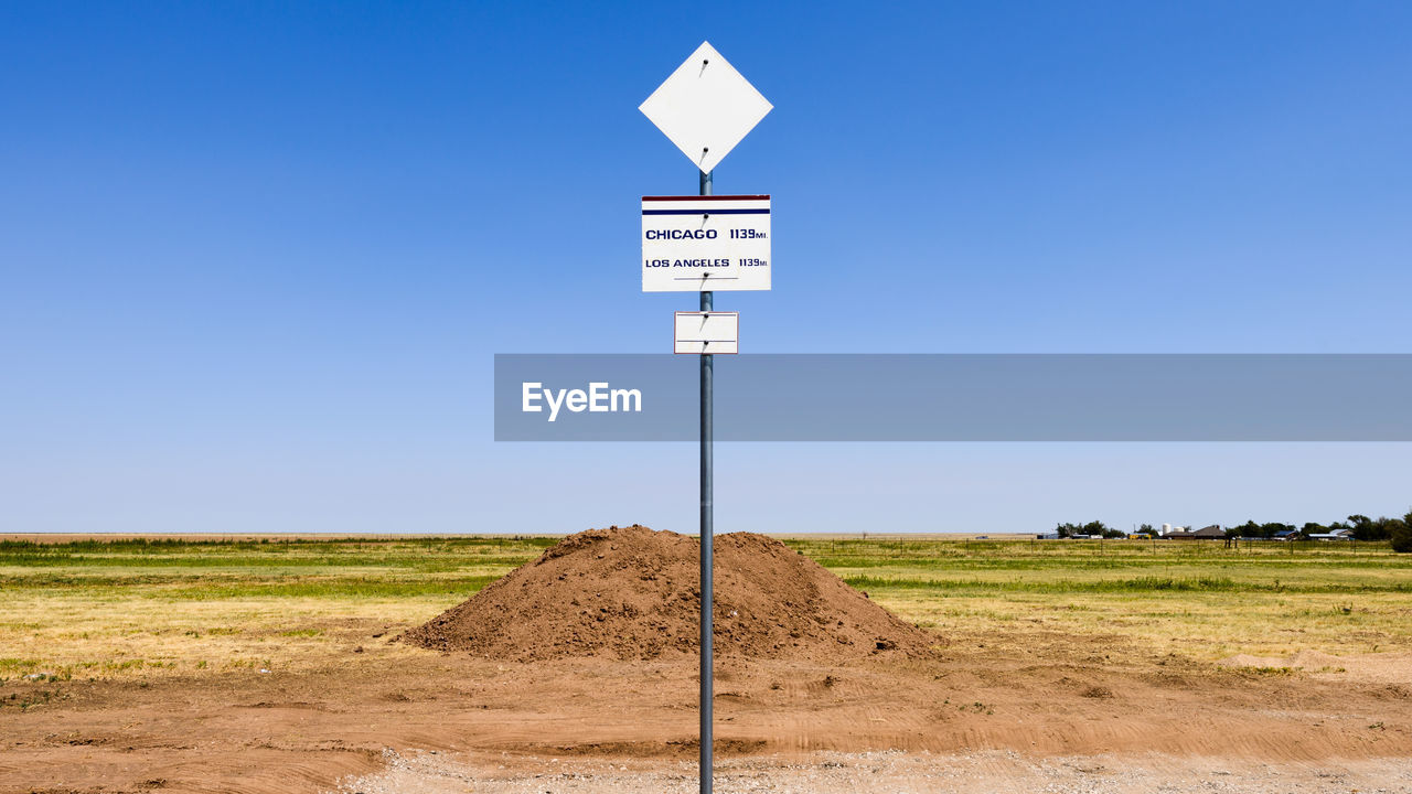 Road sign on field against clear sky