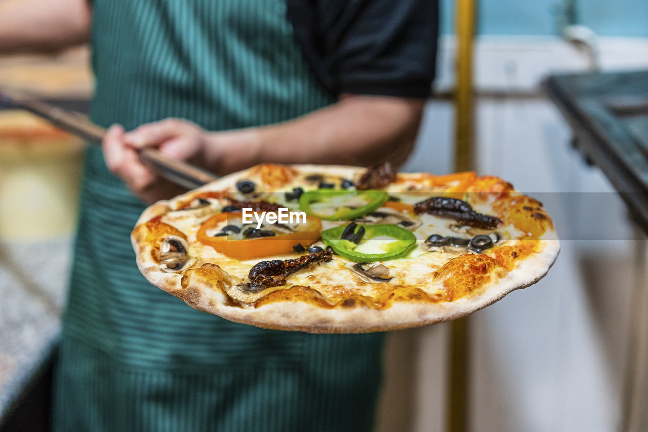 Mid section of chef holding peel with freshly made pizza