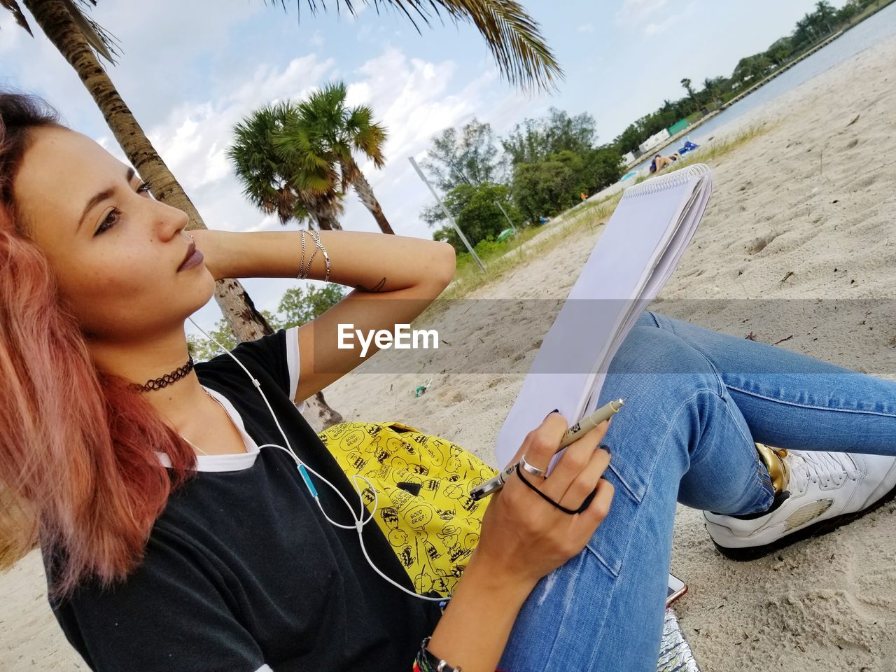 Young woman with note pad sitting on sand