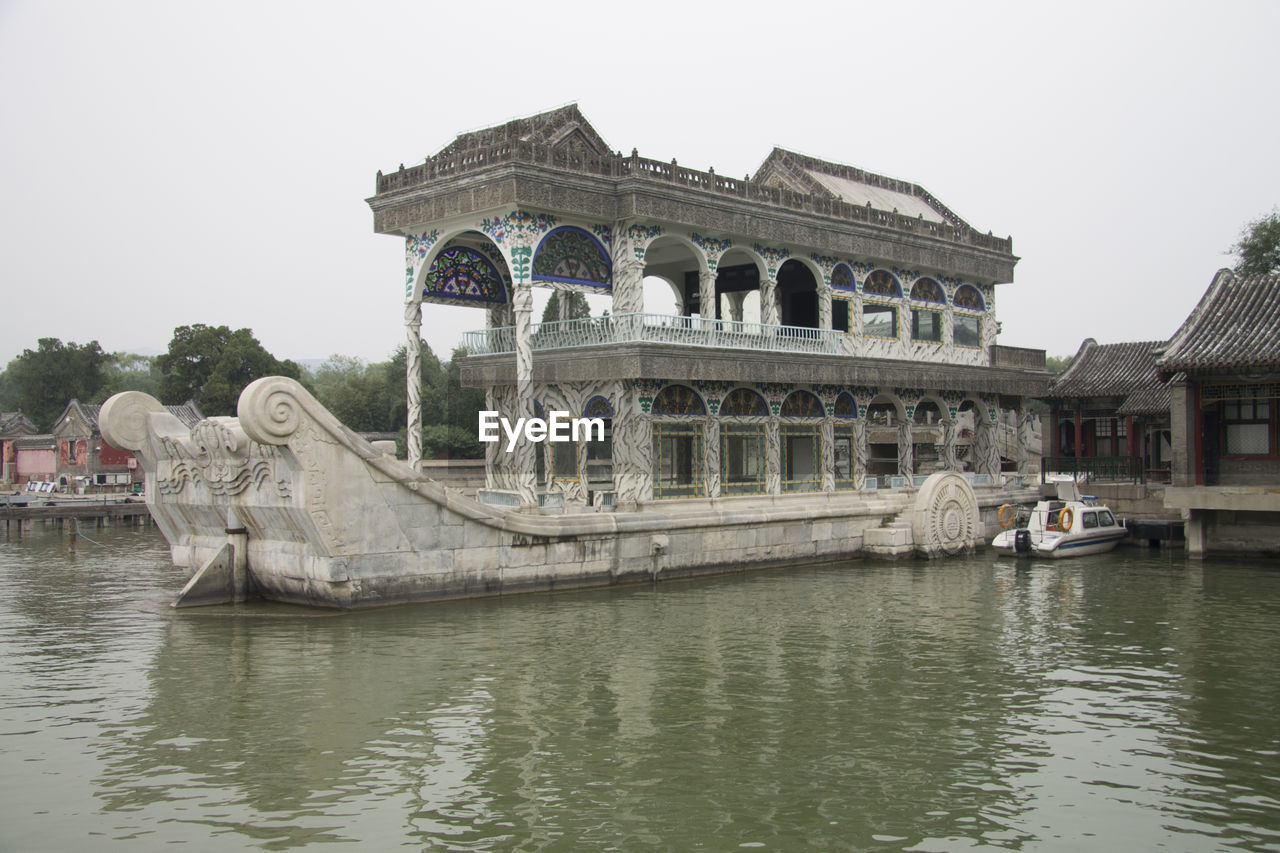 Old boat shaped building by lake against clear sky