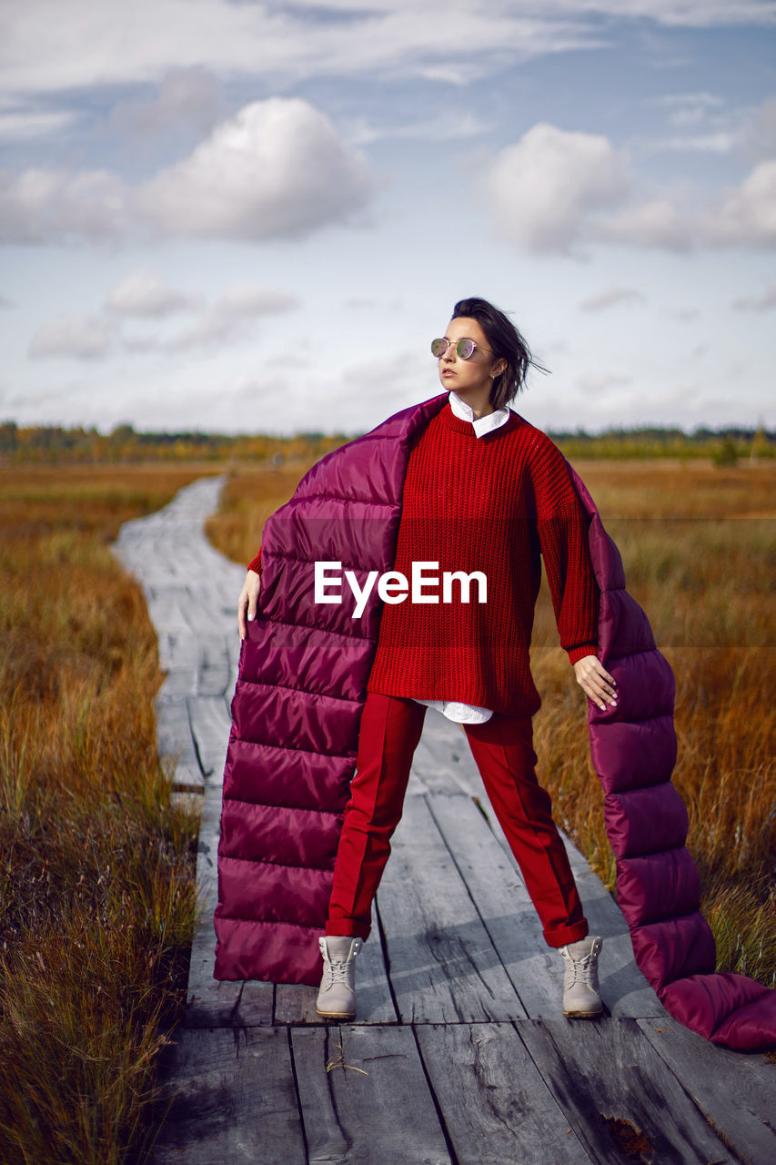 Woman  in red warm clothes and a big scarf on an ecological trail in the autumn not a swamp