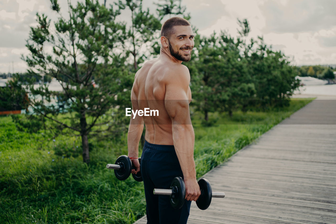 Portrait of shirtless man lifting dumbbells in park