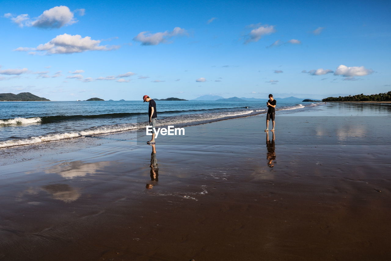 Friends standing on shore at beach against sky