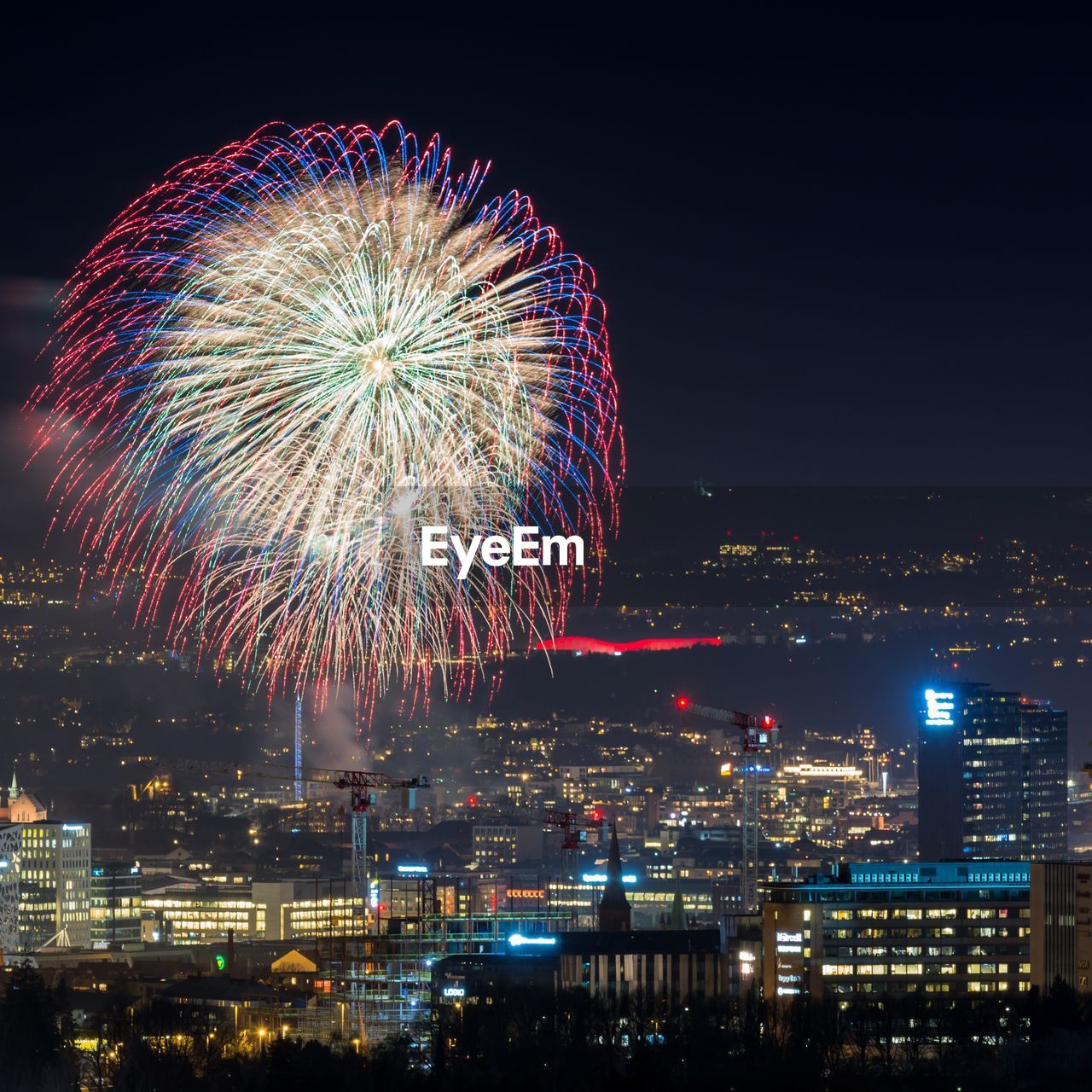 FIREWORK DISPLAY OVER ILLUMINATED BUILDINGS AGAINST SKY