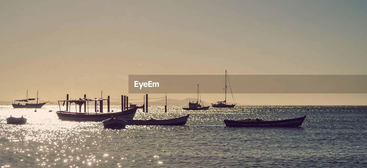 Sailboats moored in sea against clear sky during sunset