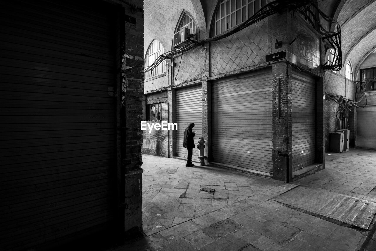 Man standing by closed shutter on footpath 