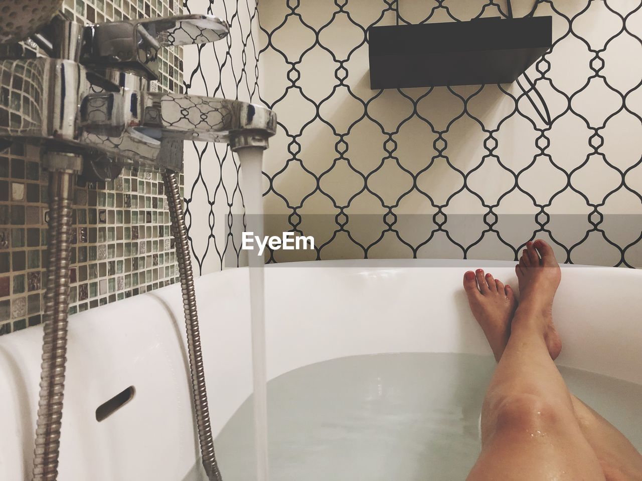 Low section of woman relaxing in bathtub at bathroom