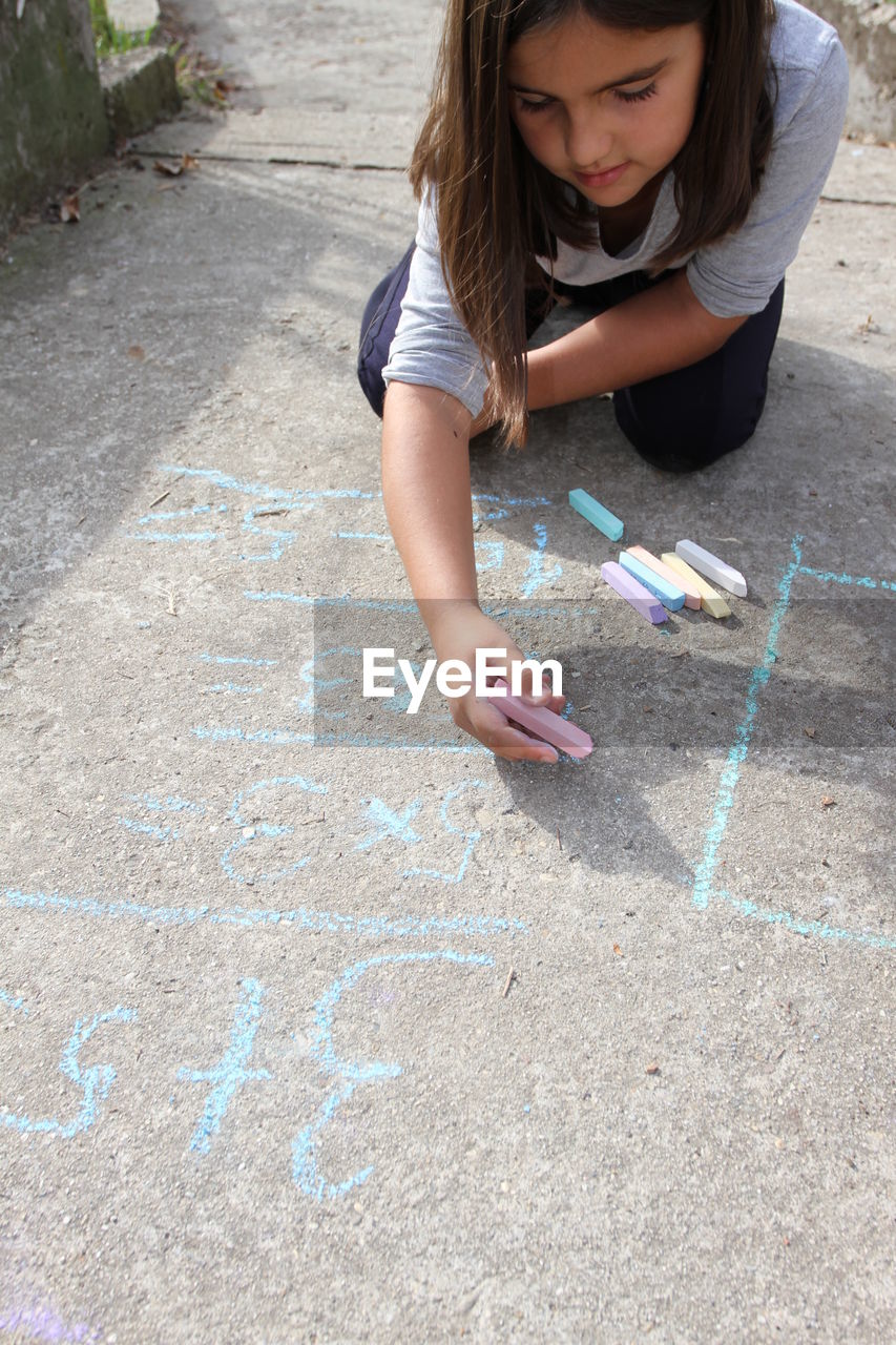 High angle of girl writing with chalk on footpath