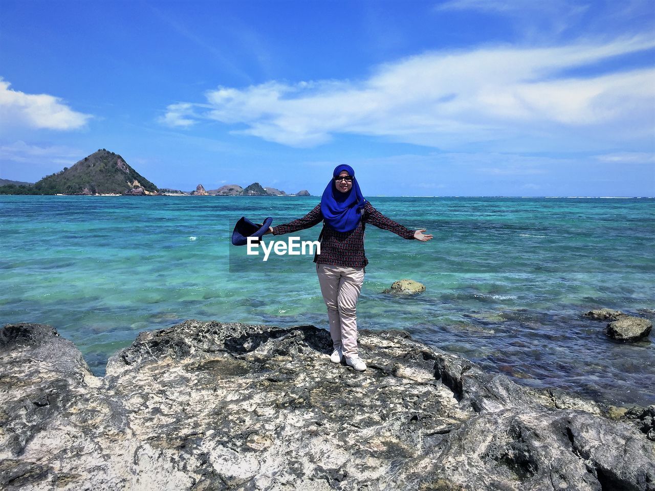 Full length of young woman standing on rock by sea against sky