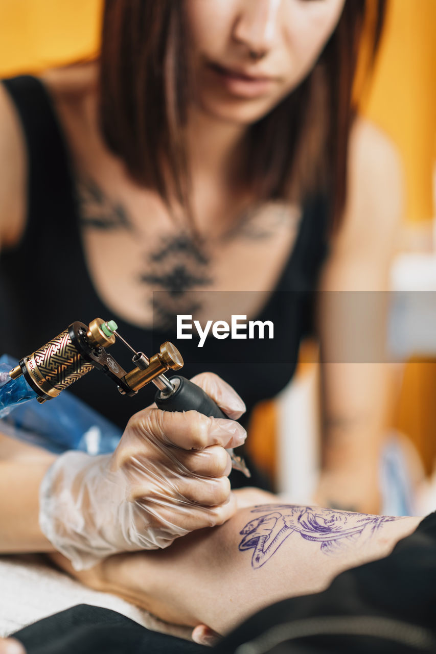 Female tattoo artist tattooing mans arm in studio