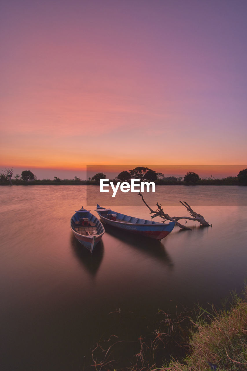 Two empty wooden boats for fishing on a calm water lake at sunset