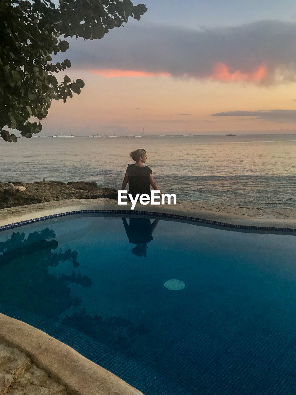 MAN IN SWIMMING POOL AGAINST SEA DURING SUNSET