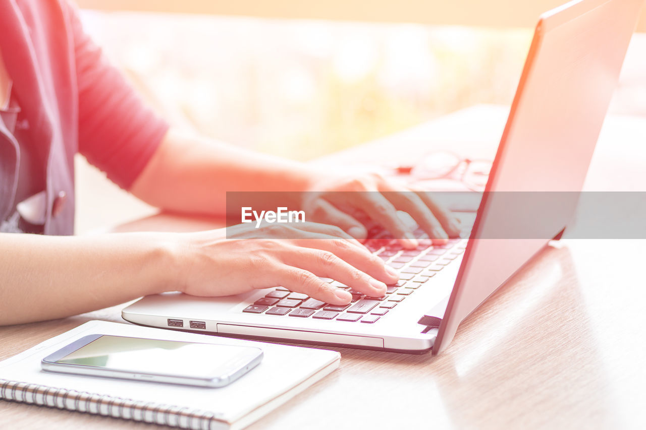 Cropped hands of businesswoman using laptop at desk in office