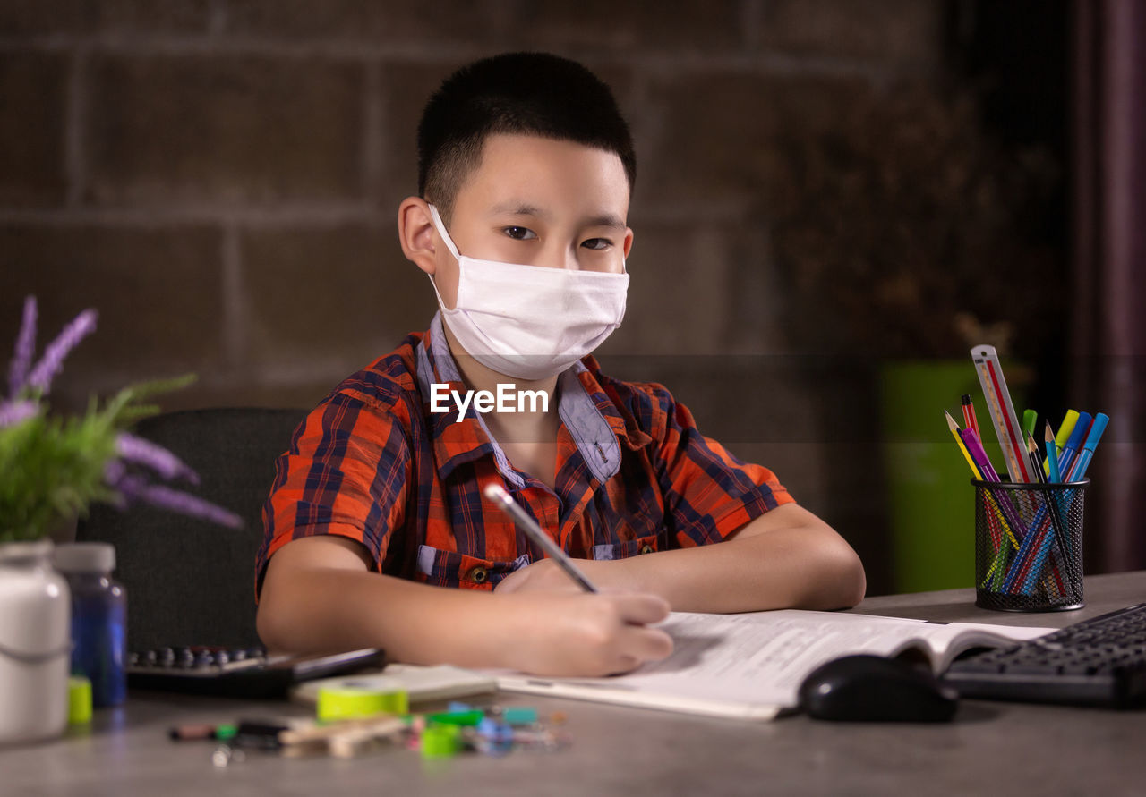 Happy boy studying with face mask on table at home