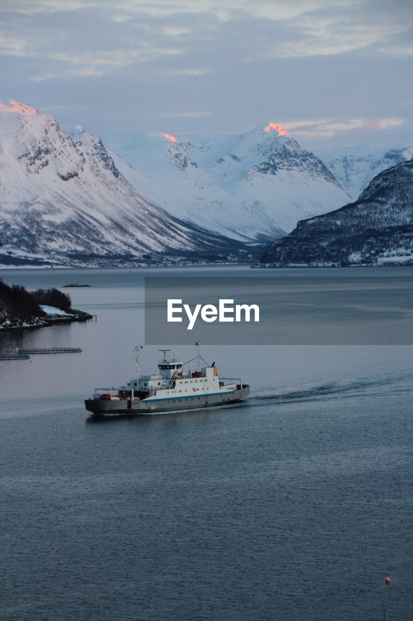 Boat sailing in river against snowcapped mountains at dusk