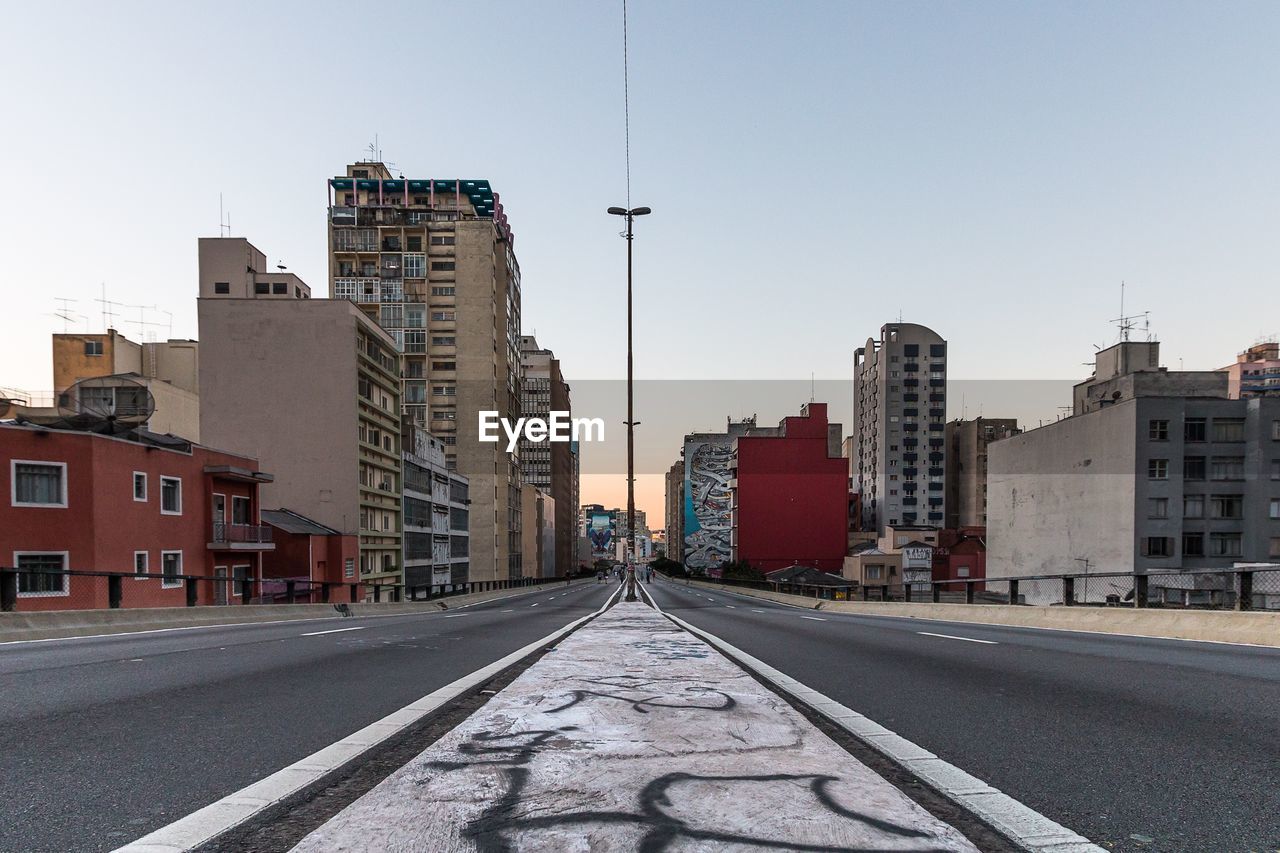 ROAD BY BUILDINGS AGAINST CLEAR SKY