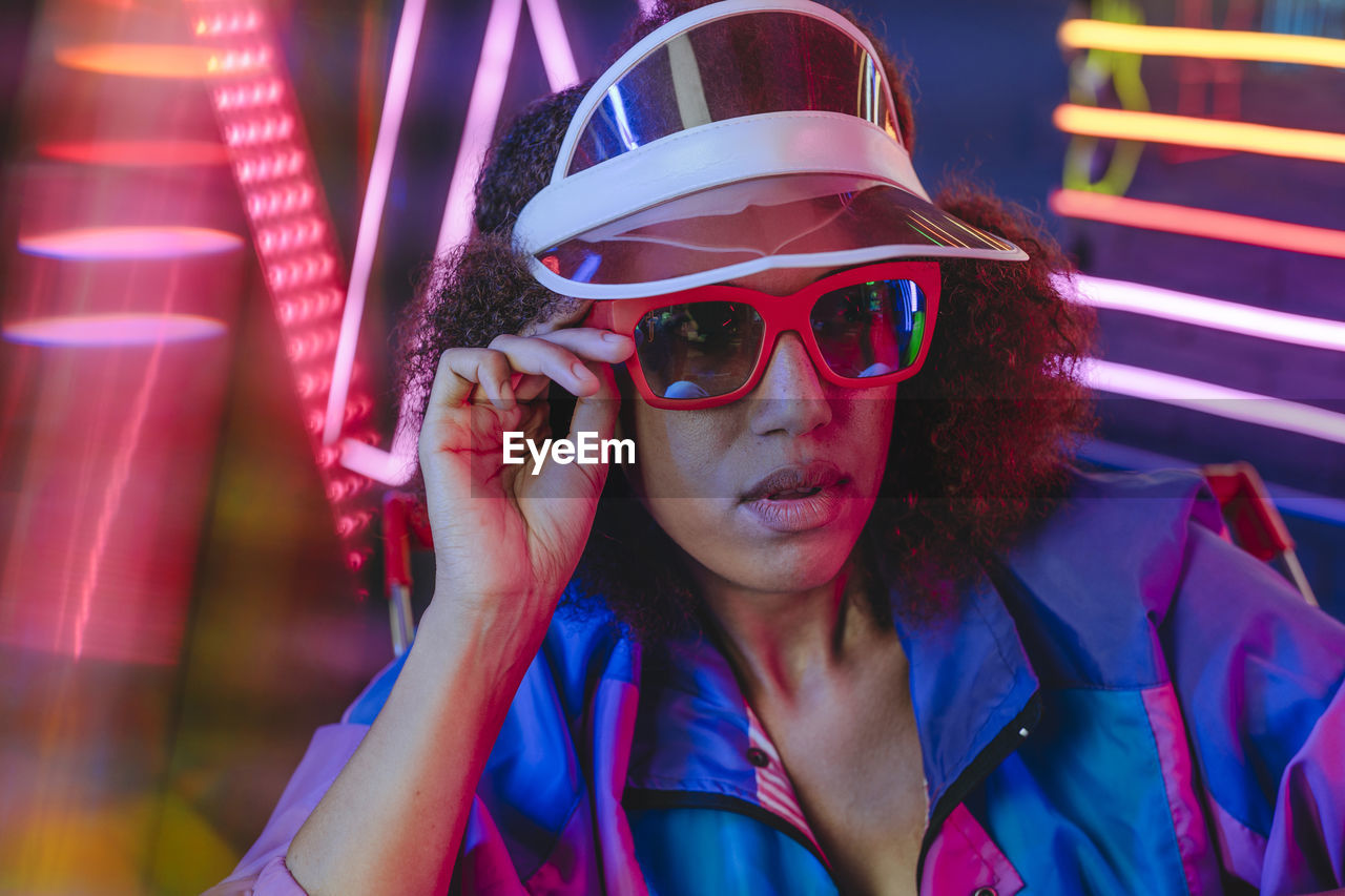 Young woman wearing retro visor and sunglasses in front of neon light