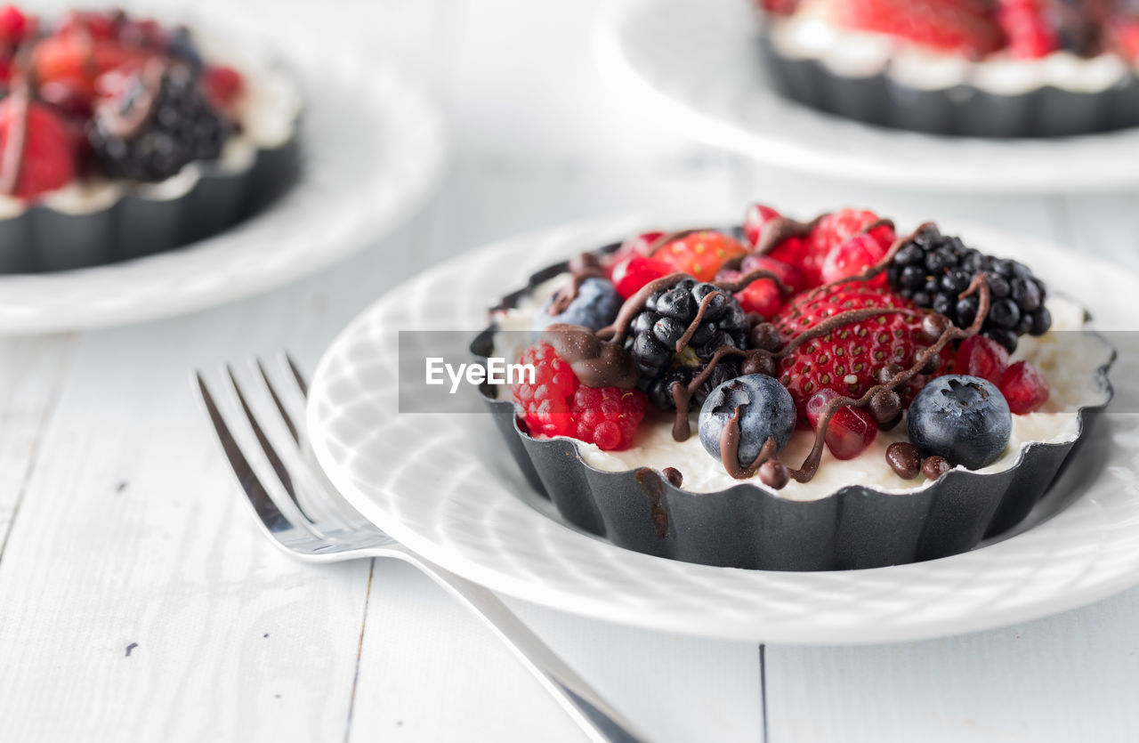 Small mixed berry cheesecake tarts drizzled with chocolate, ready for eating.