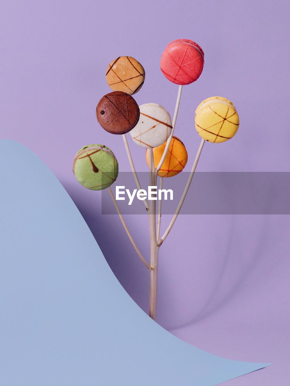 High angle view of colorful macaroons with sticks and paper on purple background