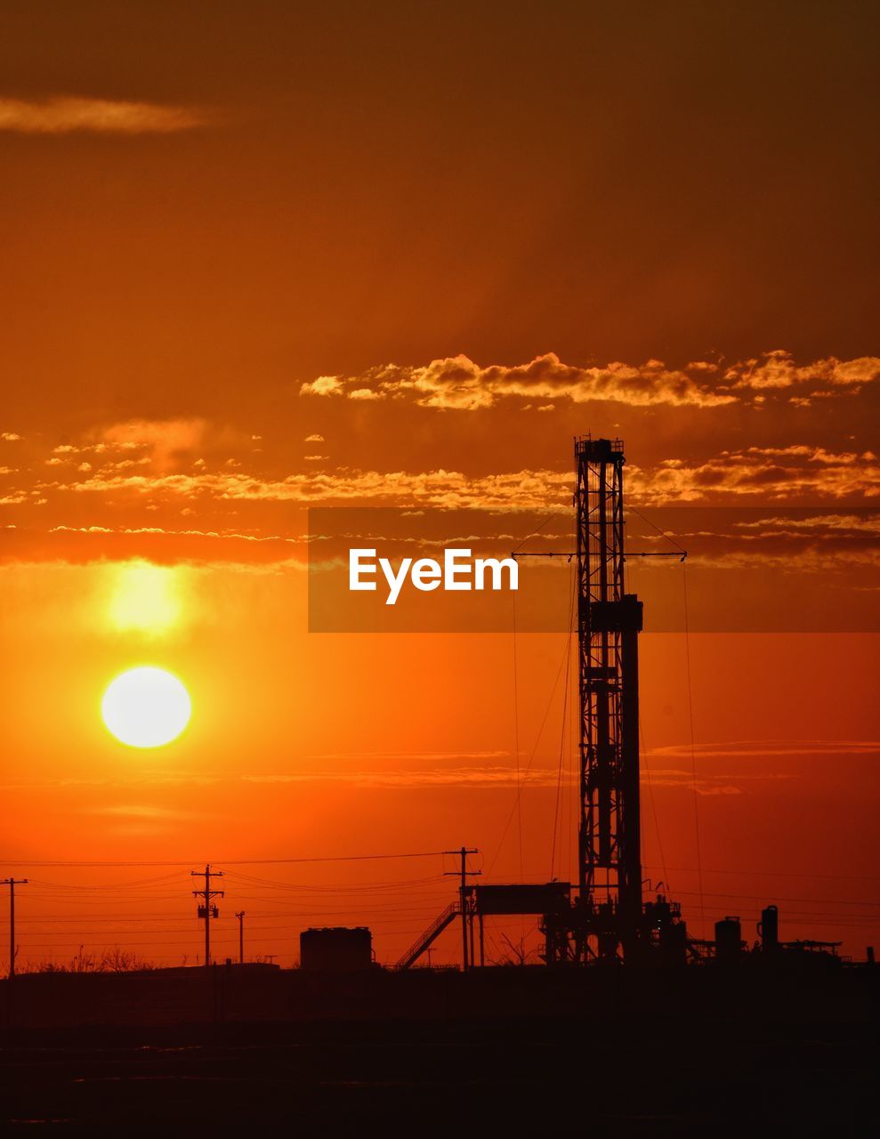 Silhouette oil pump on field against orange sky during sunset