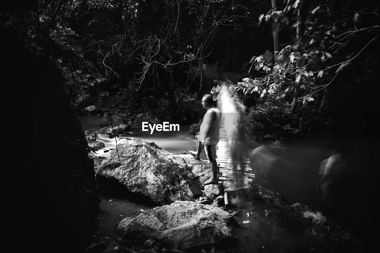 BLURRED MOTION OF PERSON STANDING ON ROCK IN FOREST