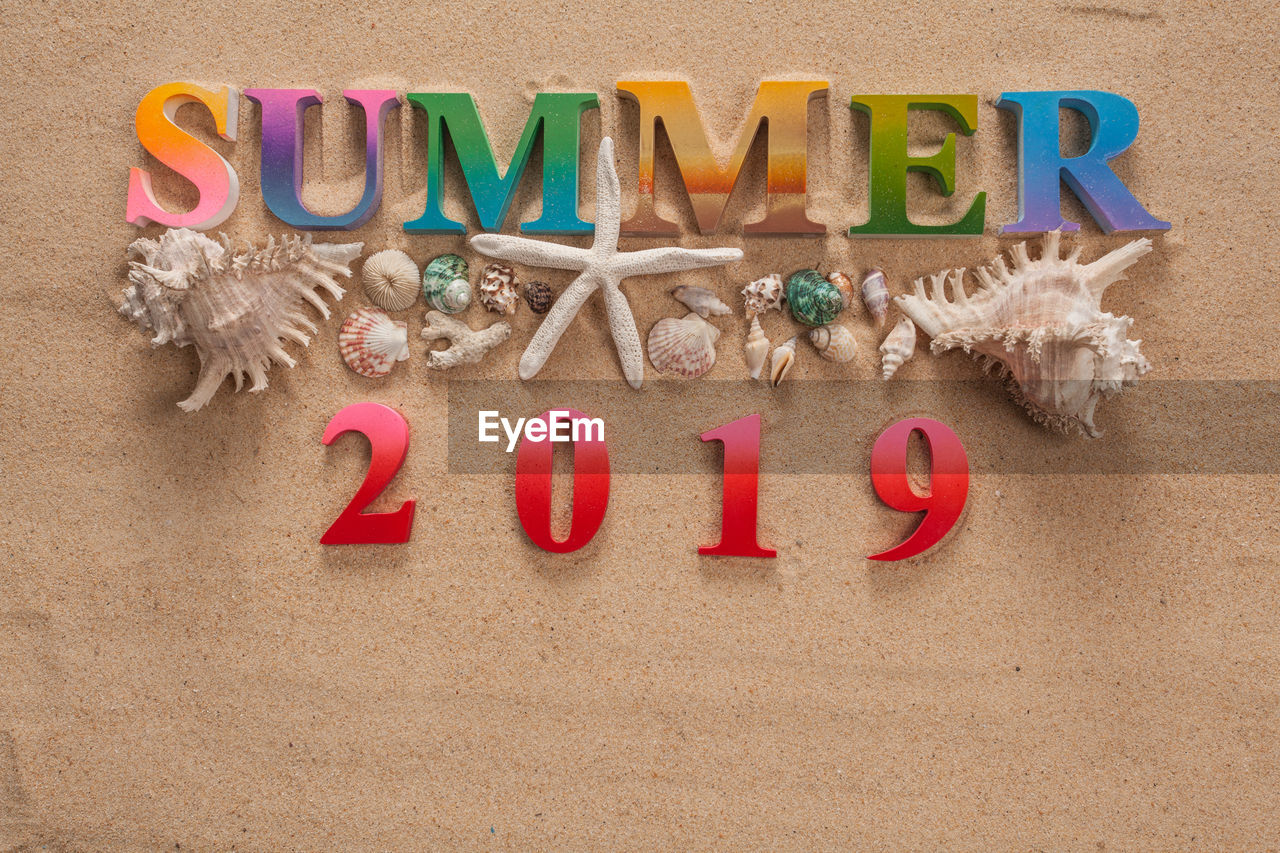 High angle view of summer text with numbers and seashells on sand at beach