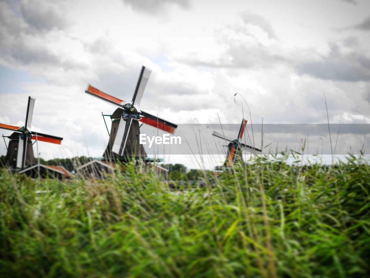 Low angle view of traditional windmills on grassy field against cloudy sky