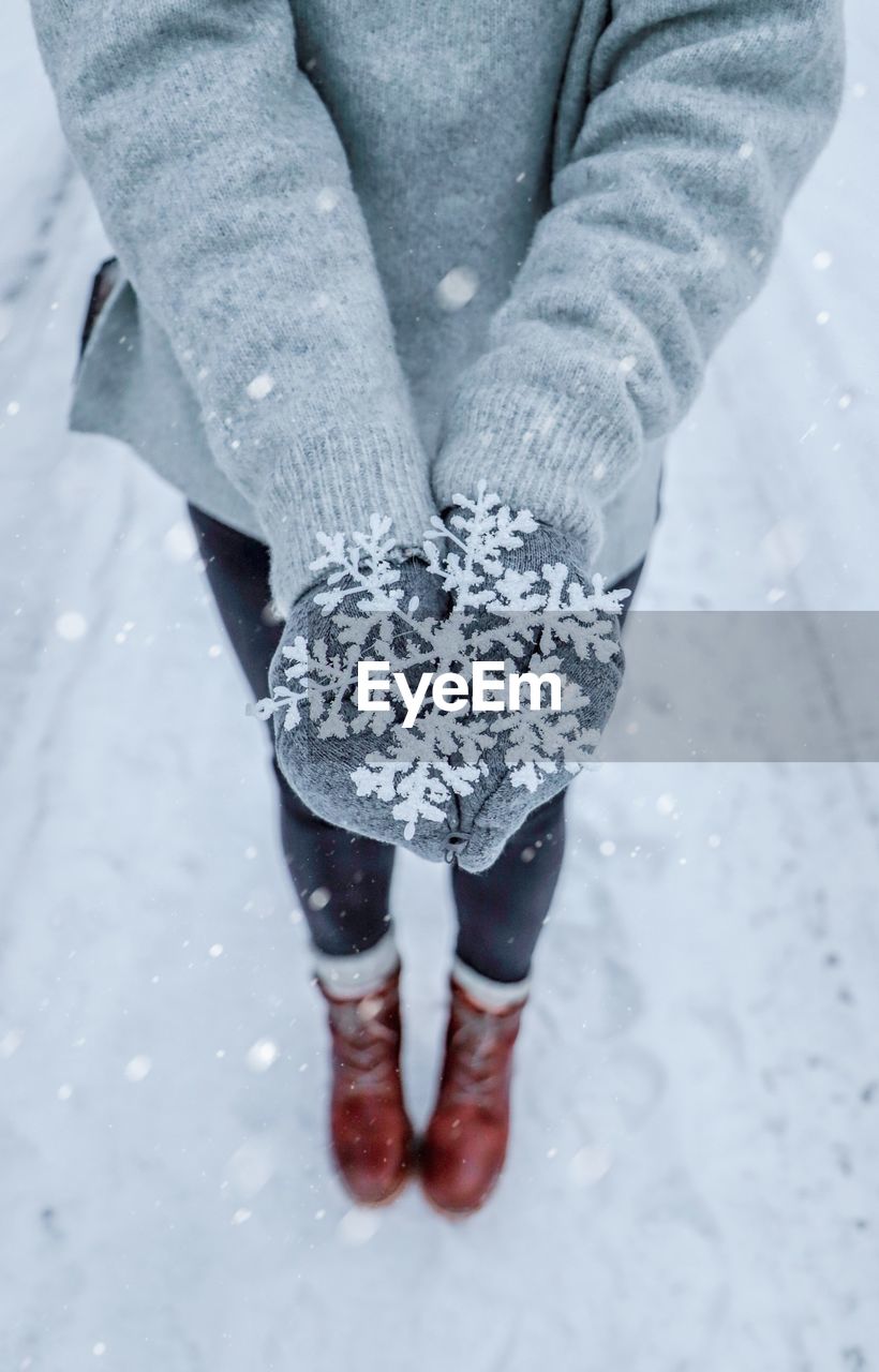 Low section of woman holding snowflakes on snow