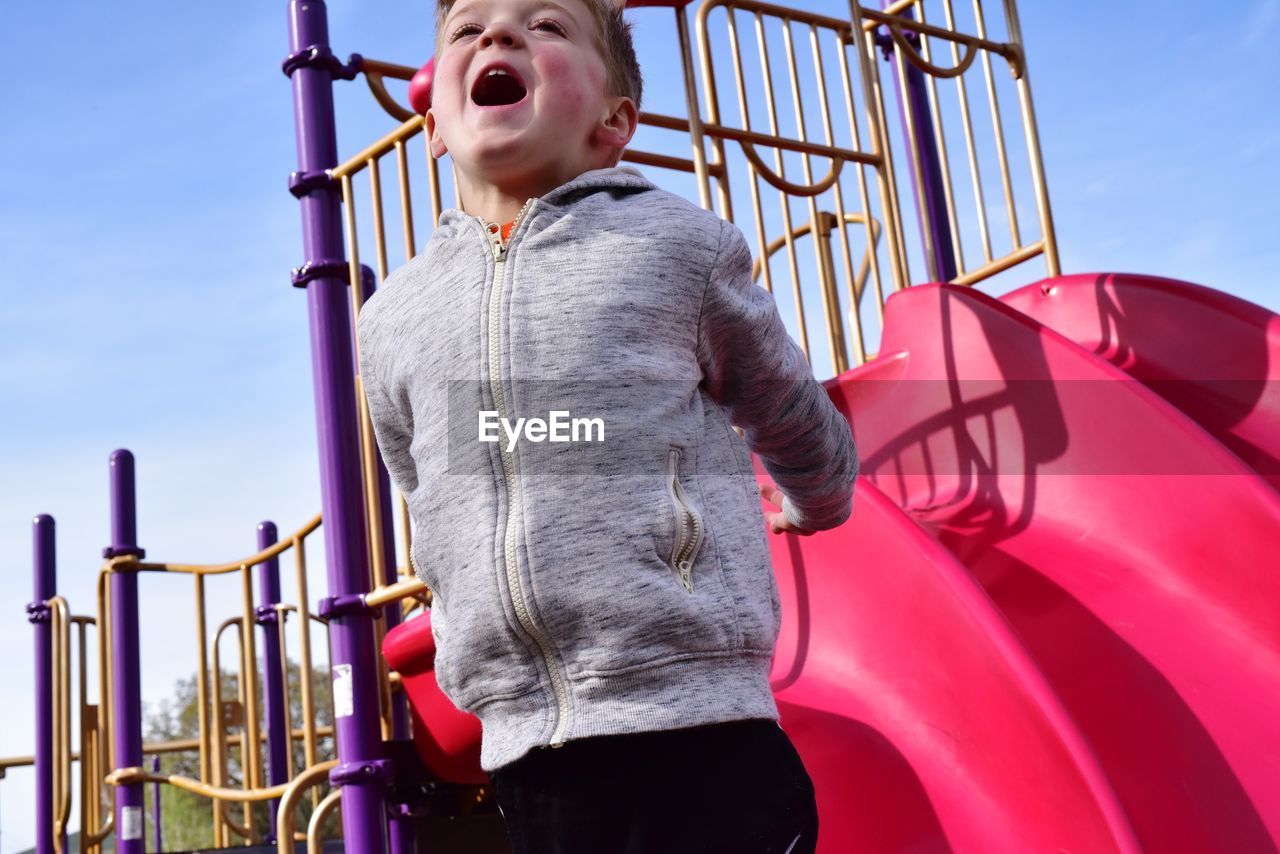 Low angle view of playful boy screaming while standing at playground