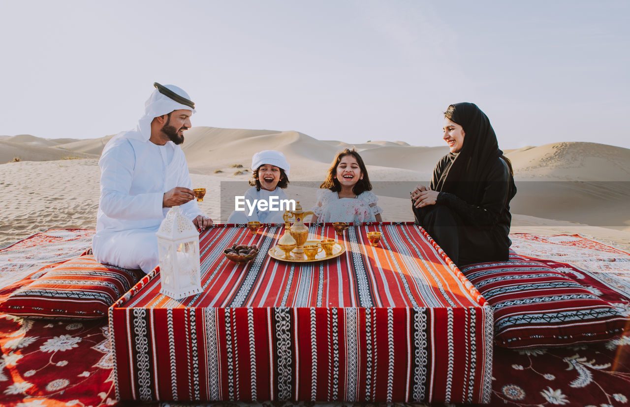 Happy family having tea on carpet at desert