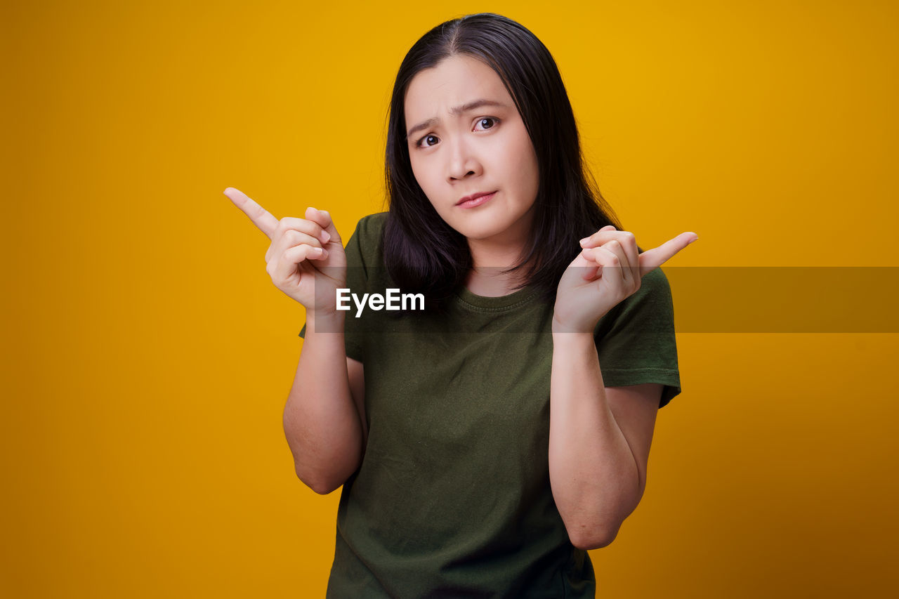 PORTRAIT OF WOMAN STANDING AGAINST YELLOW BACKGROUND