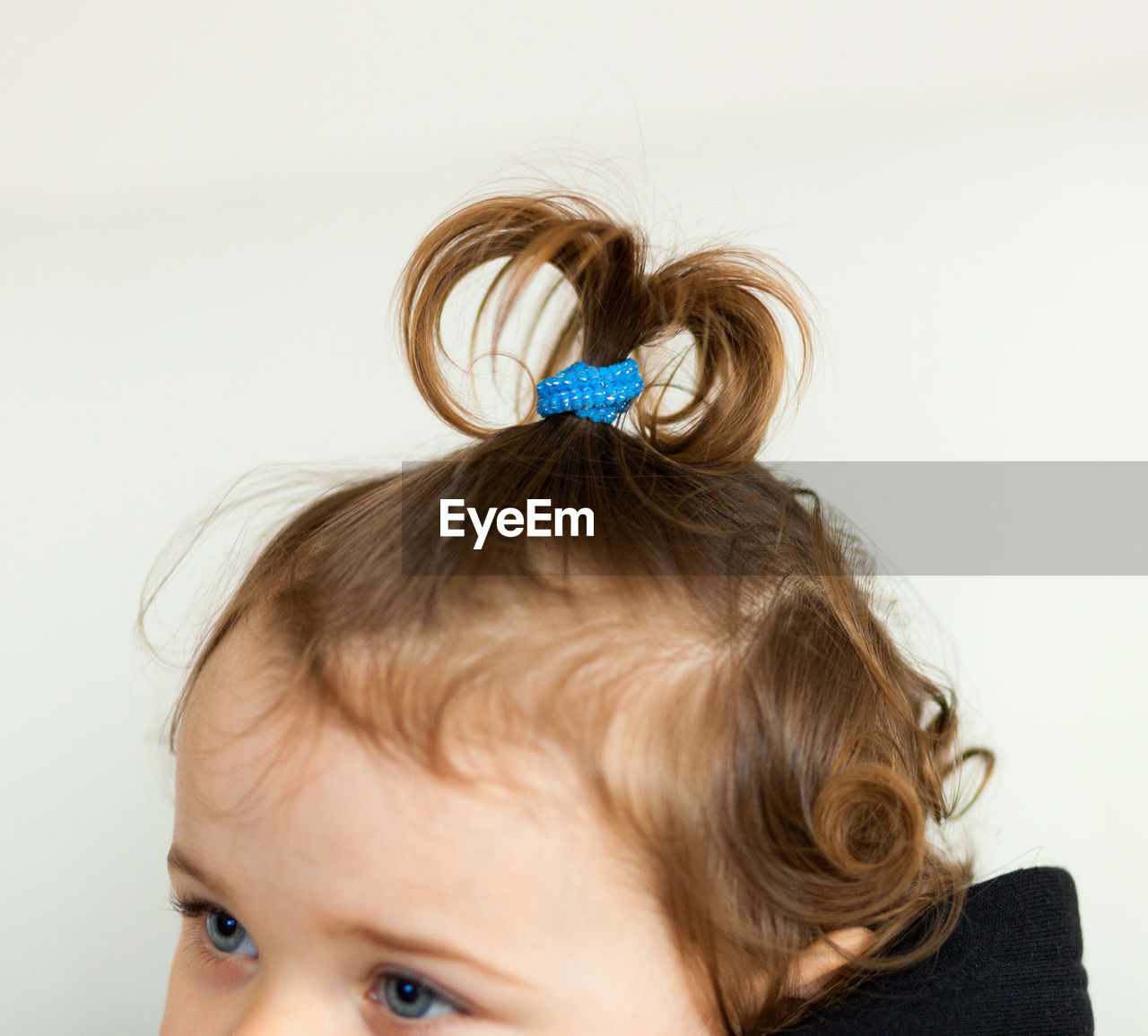 Close-up of baby girl with ponytail against wall