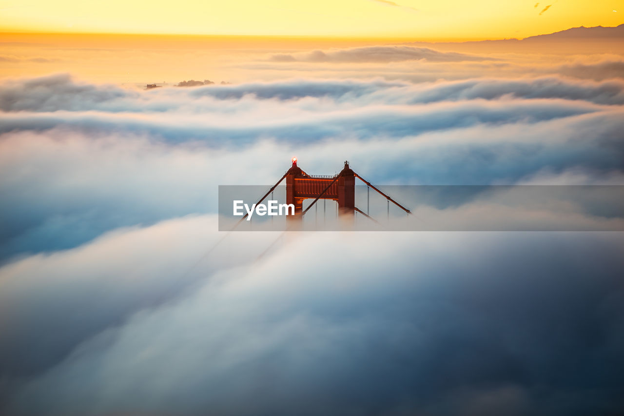 Golden gate bridge peak during fog season against sky during sunset