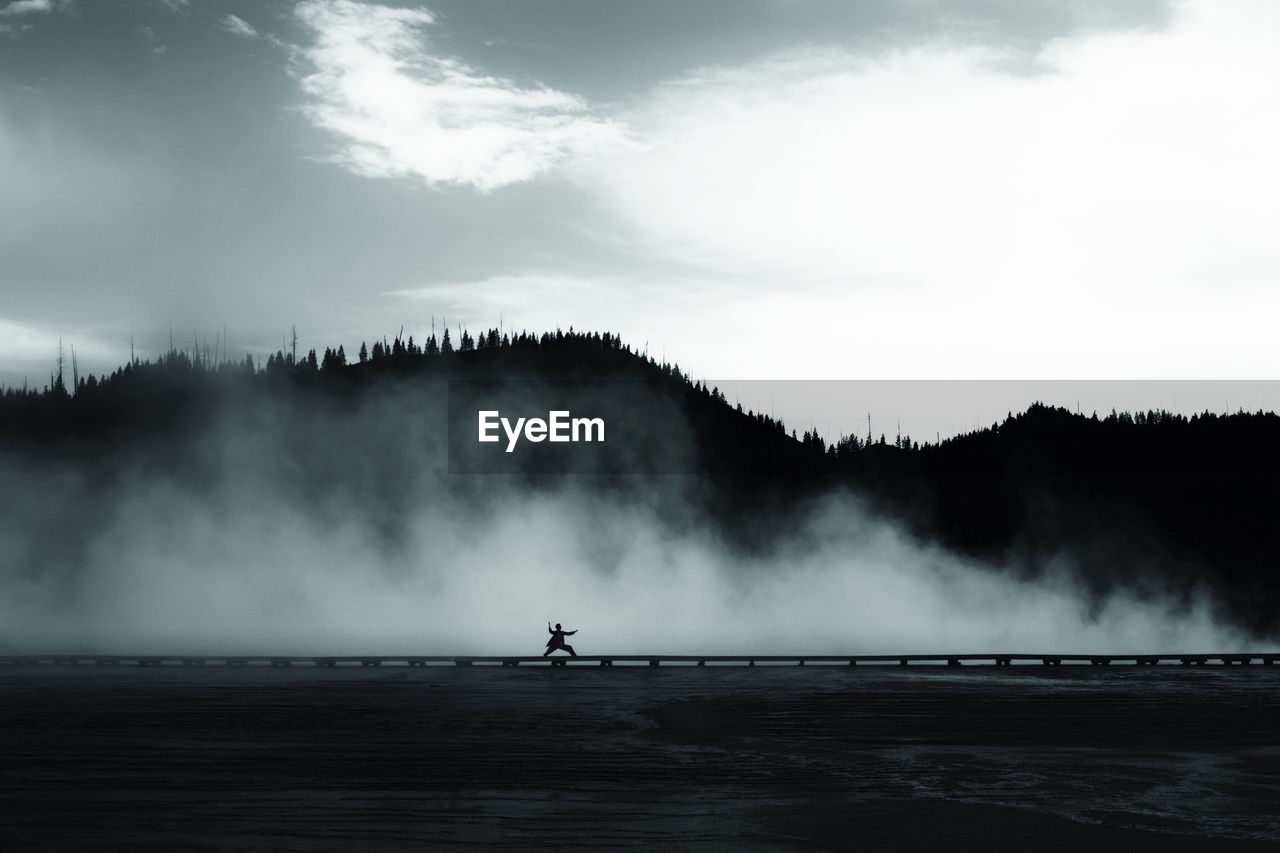 Silhouette girl doing karate by geyser at yellowstone national park against sky