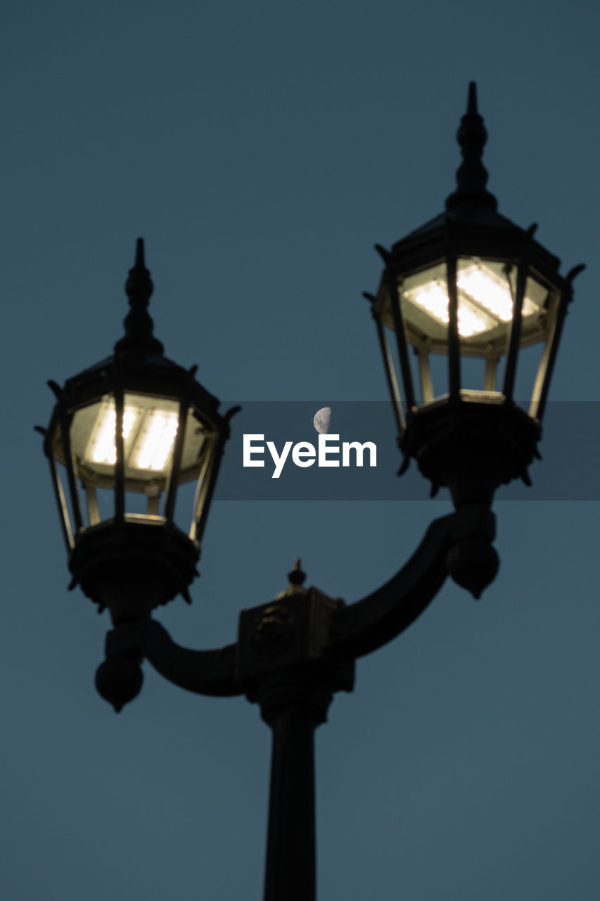 Low angle view of illuminated street light against sky with mook in background 