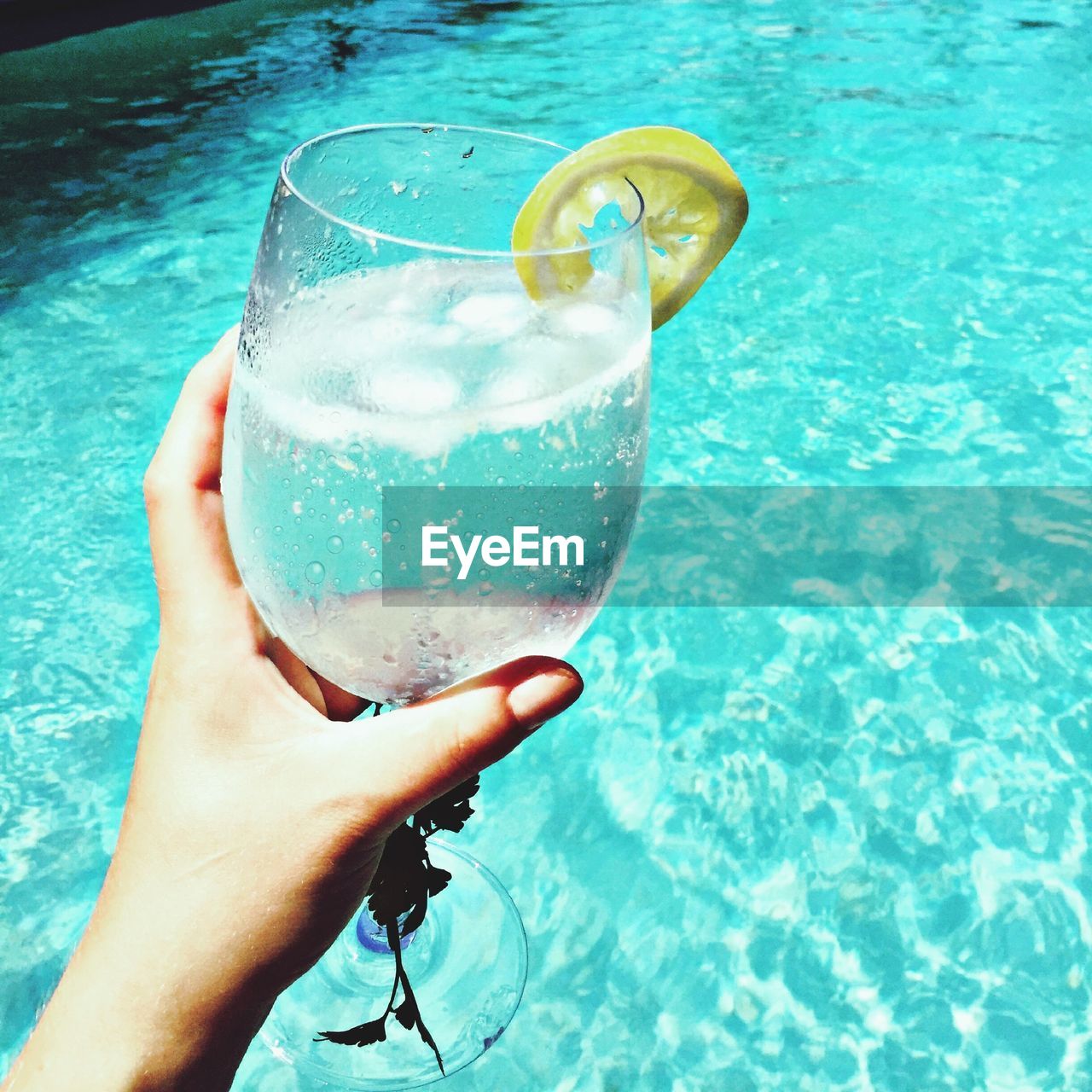 Cropped hand holding drink against swimming pool