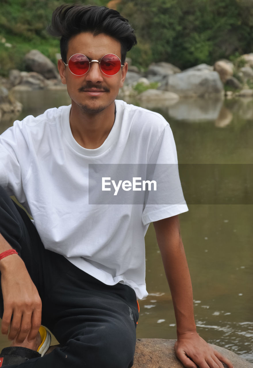 Front view of a young guy sitting in riverside with with looking at camera