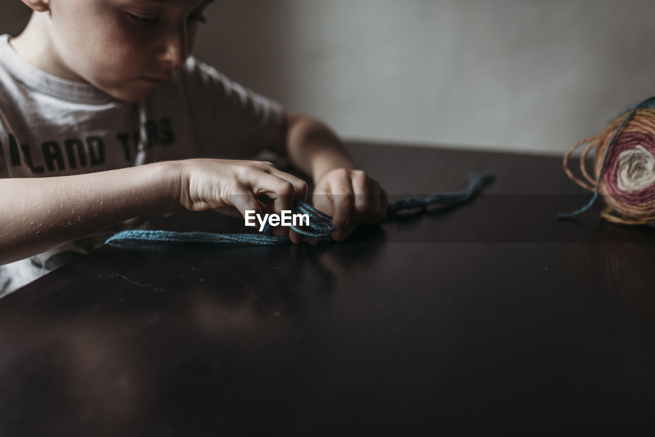 Close up of young boy knitting with fingers at home during isolation